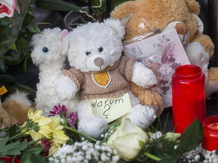 Ein Zettel mit der Aufschrift "Warum?" liegt neben Plüschtieren, Blumen und Kerzen.