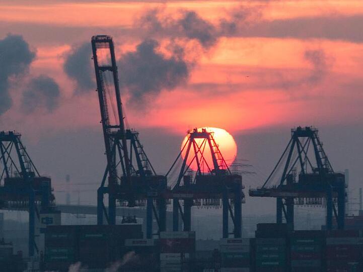 Hinter den Containerbrücken eines Terminals im Hamburger Hafen geht die Sonne unter.