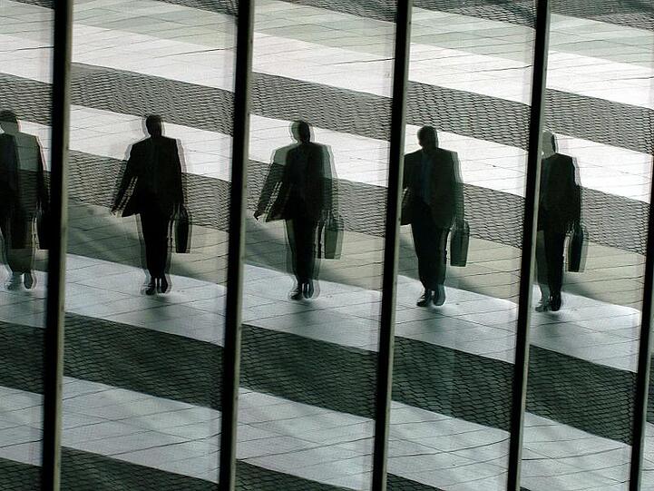 Ein Mann mit Aktentasche spiegelt sich in Glasscheiben eines Geschäftsgebäudes. Die Bundesregierung will die Übernahme deutscher Firmen durch Investoren aus Ländern außerhalb der EU künftig strenger kontrollieren.
