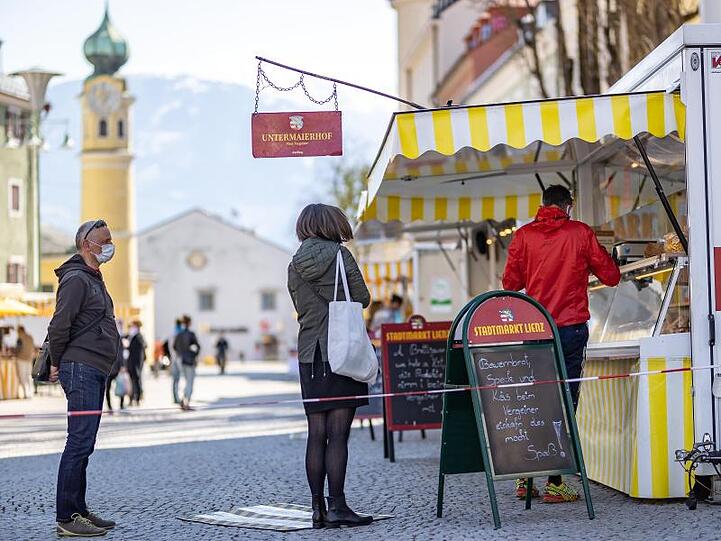 Menschen mit Mundschutz stehen an einem Marktstand in Lienz im Tirol an.