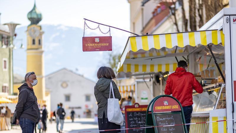 Menschen mit Mundschutz stehen an einem Marktstand in Lienz im Tirol an. Menschen mit Mundschutz stehen an einem Marktstand in Lienz im Tirol an.