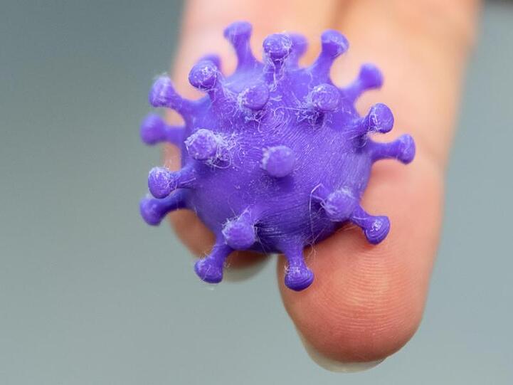 Eine Medizinisch-technische Assistentin hält auf zwei Fingern ein 3D Druck von einem Coronavirus.