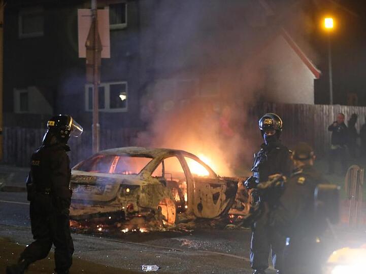 Polizisten vor einem brennenden Auto.