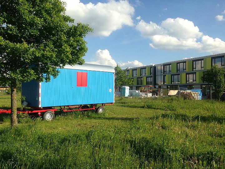 Vorne der neue Spiel-Bauwagen, hinten das Truderinger Gymnasium.