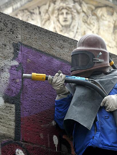Ein Arbeiter mit Schutzhelm entfernt das Graffito von der Ludwigsbrücke.