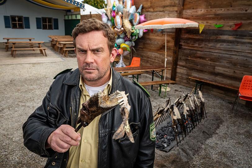 Ein toter Steckerlfischkönig beschert Niederkaltenkirchen einen neuen Mord und Franz Eberhofer (Sebastian Bezzel) seinen nächsten Fall. "Steckerlfischfiasko" ist ab 13. August 2026 im Kino zu sehen. Ein toter Steckerlfischkönig beschert Niederkaltenkirchen einen neuen Mord und Franz Eberhofer (Sebastian Bezzel) seinen nächsten Fall. "Steckerlfischfiasko" ist ab 13. August 2026 im Kino zu sehen.