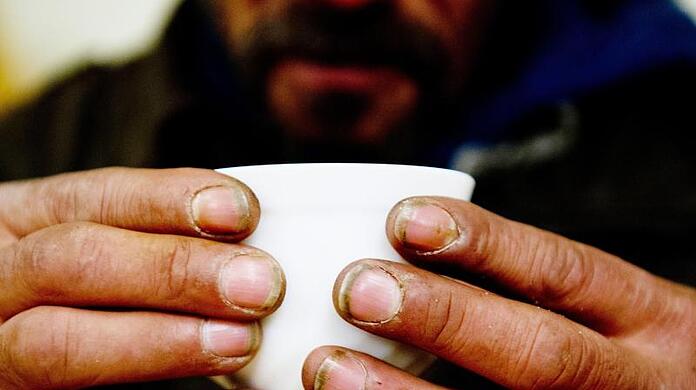 Ein obdachloser Mann hält in einem Nachtcafé eine Tasse. Viele Städte müssen wegen der Coronapandemie mehr Räume anmieten.