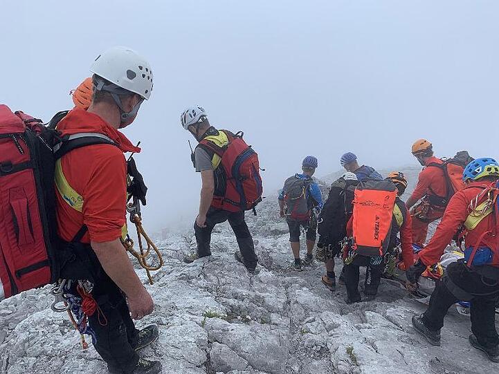 Bergretter transportieren in Nebel eine am Watzmann abgestürzte Bergsteigerin auf einer Trage den Berg hinunter. Foto: Bayerisches Rotes Kreuz