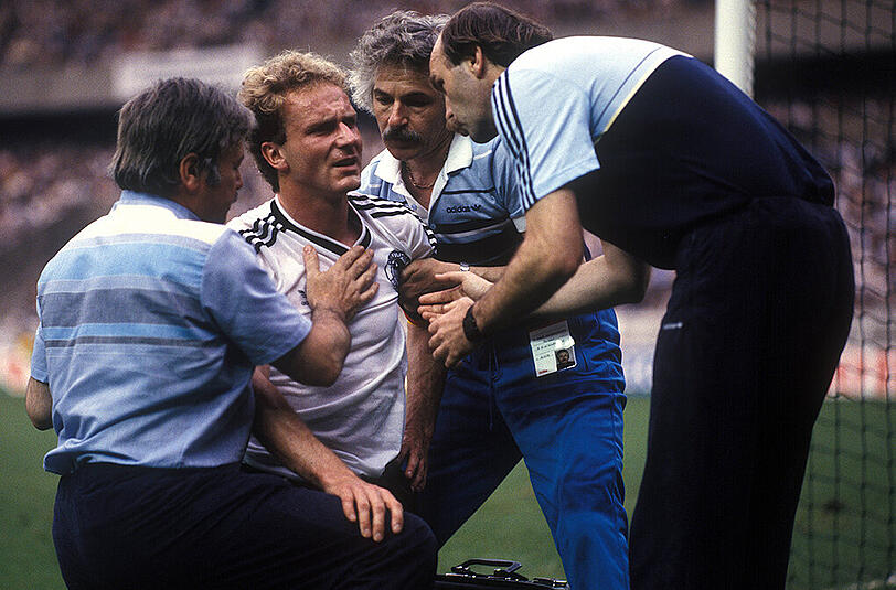 Der angeschlagene Nationalspieler Karl-Heinz Rummenigge wird während der EM 1984 in Frankreich während der Partie gegen Spanien behandelt. Rechts Co-Trainer Horst Köppel, daneben Physio Adolf Katzenmeier, links Mannschaftsarzt Dr. Heinrich Heß.