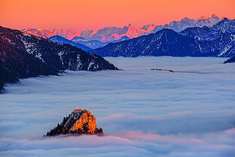 Ein Bild wie ein Märchen: Aufgenommen von der Hochplatte in den Ammergauer Alpen ragt die Spitze des Leonhardsteins aus dem Novembernebel. Dahinter glühen der Wilde Kaiser und die Loferer Steinberge im Abendlicht.