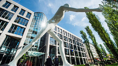Mitarbeiter gehen an der Statue &bdquo;Walking Man&ldquo; vorbei in die Zentrale der Munich Re. Berufseinsteiger erhalten dort mindestens ein Bruttogehalt in H&ouml;he von 3145 Euro im Monat.