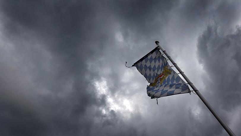 Eine Bayernfahne weht vor dichten Regenwolken im Wind.
