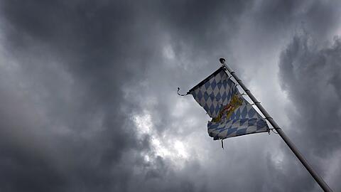 Eine Bayernfahne weht vor dichten Regenwolken im Wind.