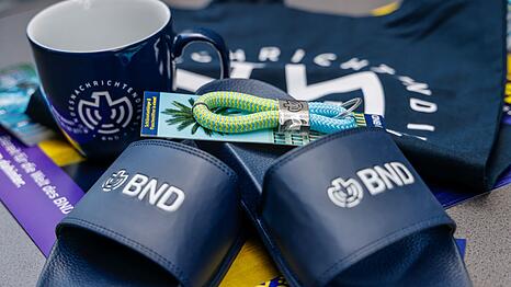 Im Merchandise-Shop gibt es T-Shirts und auch Badelatschen mit BND-Logo.