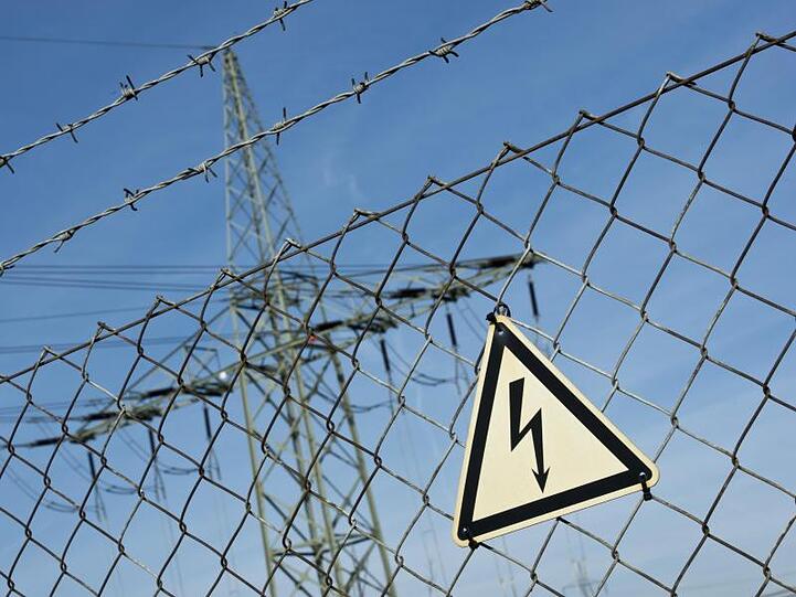 Ein Gefahrenschild für Elektrizität ist vor einer Stromtrasse zu sehen. Foto: Daniel Naupold/Archiv