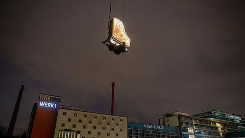 Der Künstler Alain Roche sitzt an seinem beleuchteten Flügel, der an einem Kran gehalten wird.