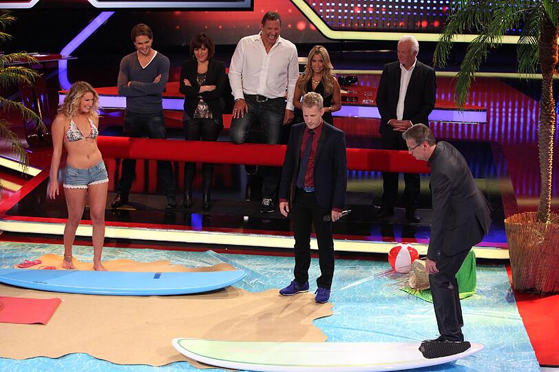 Janni Hönscheid, die deutsche Meisterin im Wellenreiten 2013, zeigt Günther Jauch wie man auf dem Board Balance hält. In der Mitte Moderator Oliver Pocher.