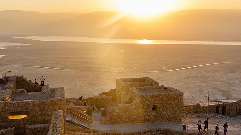 Über dem Toten Meer geht die Sonne auf und bestrahlt die Festung Masada.