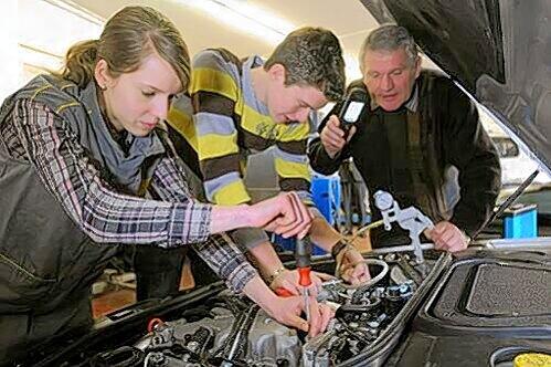 Zwei Mechatroniker-Azubis arbeiten unter Anleitung ihres Meisters am Motor eines Mercedes-E-Klasse-Modells. Mechatroniker ist ein gefragter Lehrberuf.