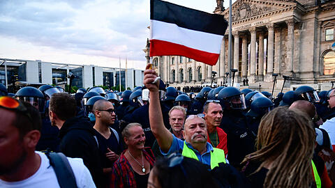 Teilnehmer einer Kundgebung gegen die Corona-Maßnahmen. Ein Teilnehmer hält eine Reichsflagge.