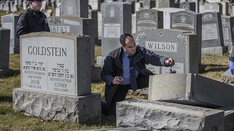 Ein Polizist nimmt auf dem geschändeten jüdischen Mount Carmel Friedhof Fingerabdrücke von Grabsteinen.