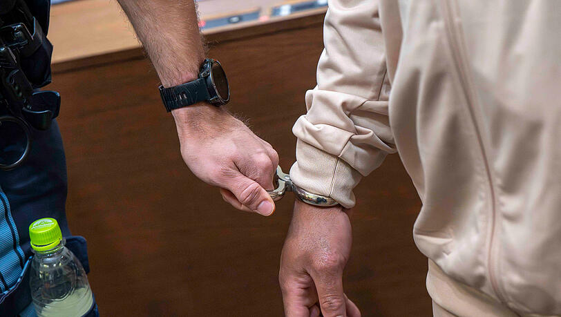 Ein mutmaßliches Mitglied der nigerianischen Mafia (r) wird zu Prozessauftakt in Handschellen in den Gerichtssaal geführt. Ein mutmaßliches Mitglied der nigerianischen Mafia (r) wird zu Prozessauftakt in Handschellen in den Gerichtssaal geführt.