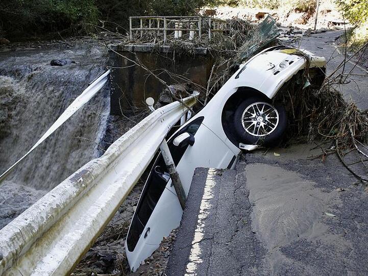 Ein Auto hängt an einer eingestürzten Straße über einem Fluss fest.