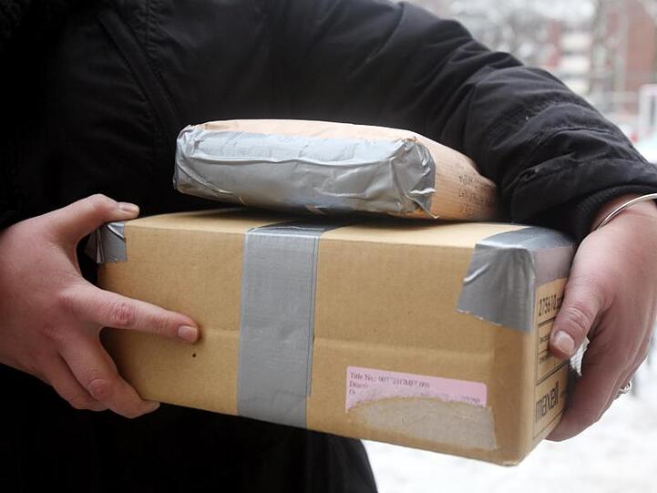 Eine Frau trägt Pakete zu einer Postfiliale.