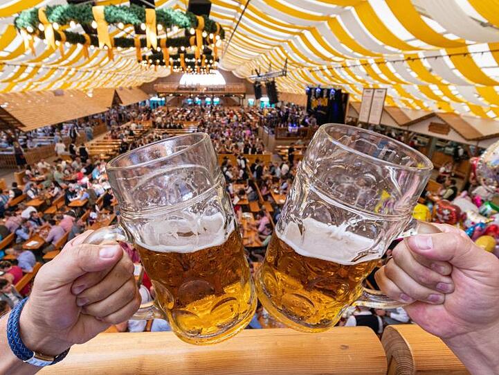 Besucher des Gäubodenvolksfestes stoßen in einem Festzelt mit Bierkrügen an. Foto: Armin Weigel/Archivbild
