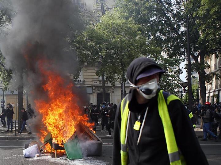 Ein Anhänger der "Gelbwesten" geht in Paris während einer Demonstration an brennenden Gegenständen vorbei.