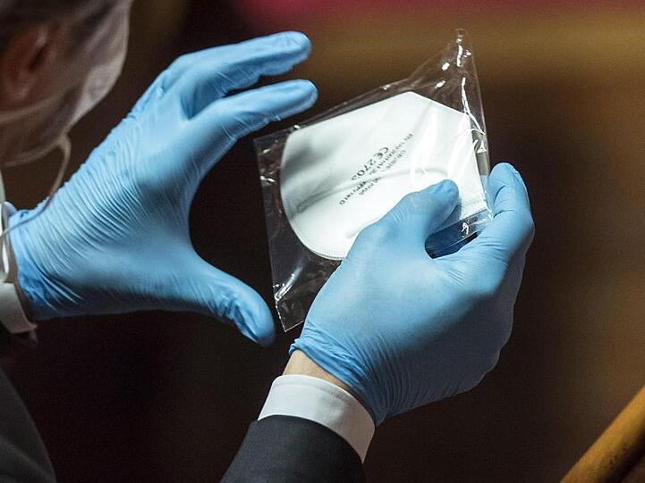 Ein italienischer Parlaments-Abgeordneter mit Gummihandschuhen hält eine verpackte Mundschutzmaske in den Händen.