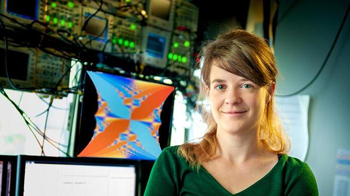 Die Experimentalphysikerin Monika Aidelsburger steht vor Bildschirmen in einem Labor.