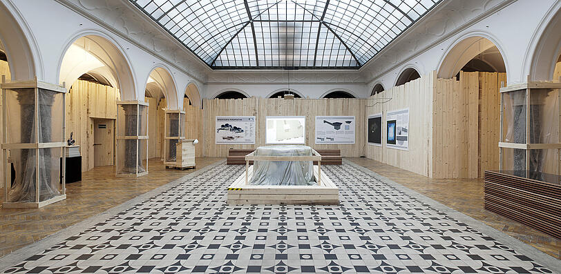 Besucher der Rathausgalerie finden einen Ort vor, der im Umbau zu sein scheint: Durch die vollständige Auskleidung des Raums mit rohen Holzwänden, auf denen vier große Bauschilder angebracht sind, wird eine Baustelle simuliert. Die Schilder zeigen die Pläne eines neuen Raums für zeitgenössische Kunst, der mit der Rathausgalerie durch einen für die Öffentlichkeit unzugänglichen Tunnel im Untergrund verbunden ist.
