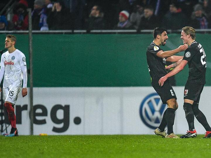 Augsburgs Rani Khedira (M) und Fredrik Jensen (r) feiern den Treffer zum 1:0-Sieg - daneben lässt der Kieler Johannes van den Bergh den Kopf hängen.