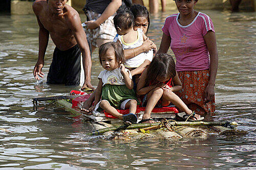 In Manila setzen Eltern ihre Kinder auf selbstgebautes Floß, um sie durch die Fluten zu bringen