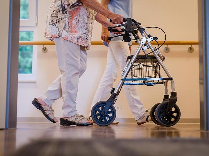 Eine Pflegekraft geht in einem Pflegeheim mit einer älteren Dame über einen Korridor.