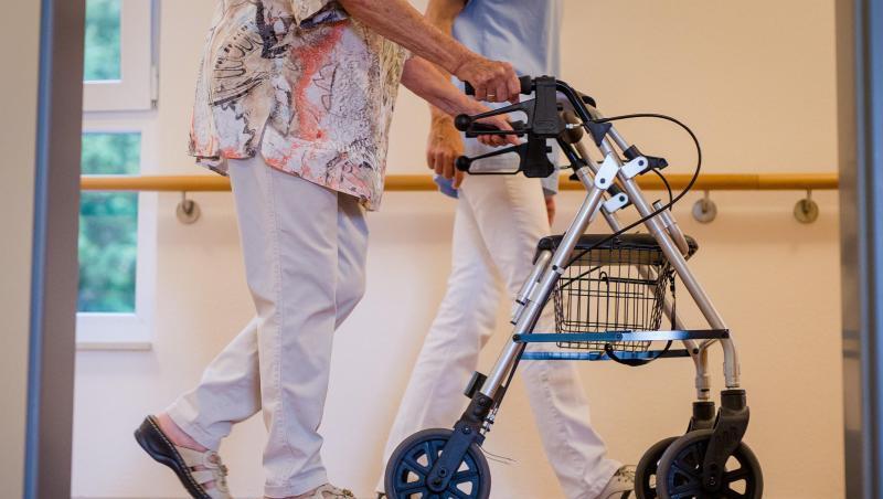 Eine Pflegekraft geht in einem Pflegeheim mit einer älteren Dame über einen Korridor. Eine Pflegekraft geht in einem Pflegeheim mit einer älteren Dame über einen Korridor.
