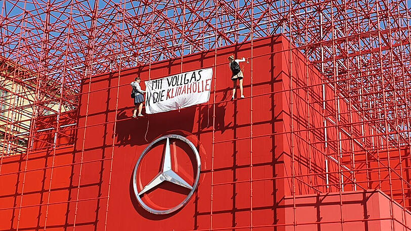 Zwei Aktivistinnen hängen ein Banner am Mercedes-Benz Showroom auf.
