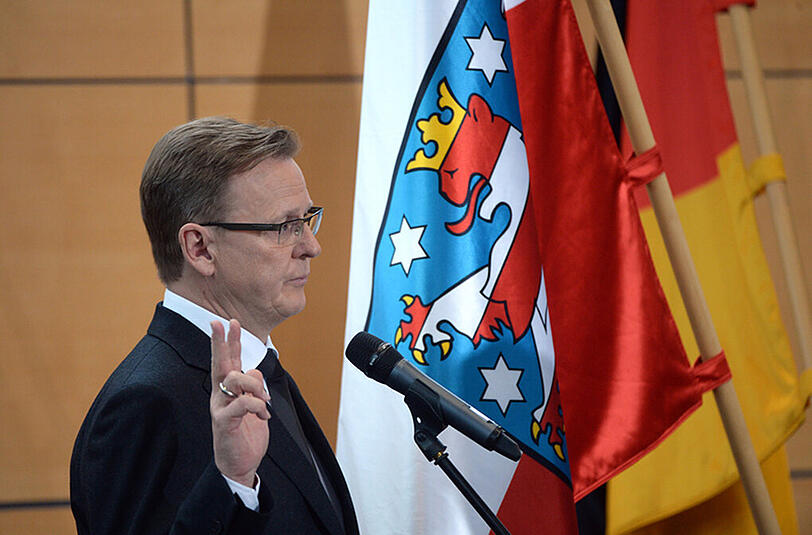 Bodo Ramelow legt vor der deutschen und der Flagge des Freistaats Thüringen den Amtseid ab.