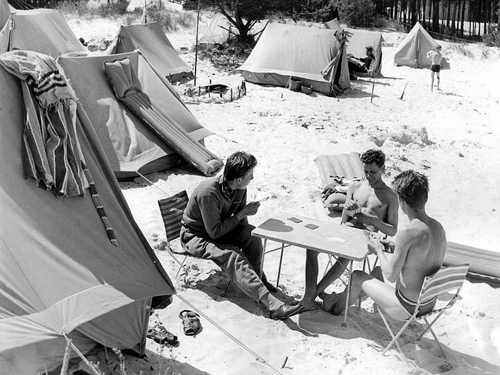 Drei Männer, die auf Klappstühlen sitzen, kloppen während ihres Urlaubs auf einem Zeltplatz an der Ostseeküste eine Runde Skat.
