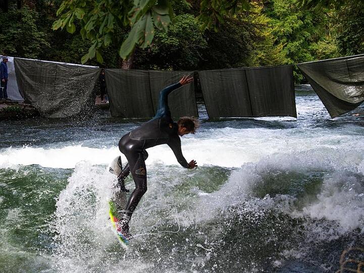 Ein Eisbachsurfer springt mit seinem Surfbrett auf die Eisbachwelle.