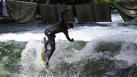 Ein Eisbachsurfer springt mit seinem Surfbrett auf die Eisbachwelle.