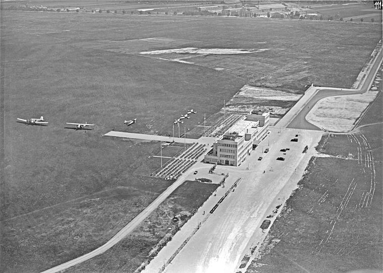 Der erste Verkehrsflughafen München eröffnet am 3. Mai 1931 am Oberwiesenfeld, wo heute der Olympiasee liegt. Bereits seit 1890 war das Rollfeld militärisch genutzt worden. Der neue Flughafen wird aber schnell zu klein, schon 1939 zieht man in den neuen Flughafen nach Riem um.