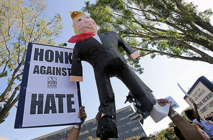 Ein Schild mit der Aufforderung "Hupe gegen Hass" - dazu eine aufblasbare Puppe, die Donald Trump darstellt.