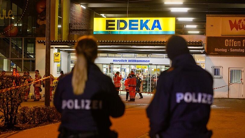 Einsatzkräfte der Polizei stehen auf einem Supermarkt-Parkplatz, vor dem Schüsse gefallen sind.
