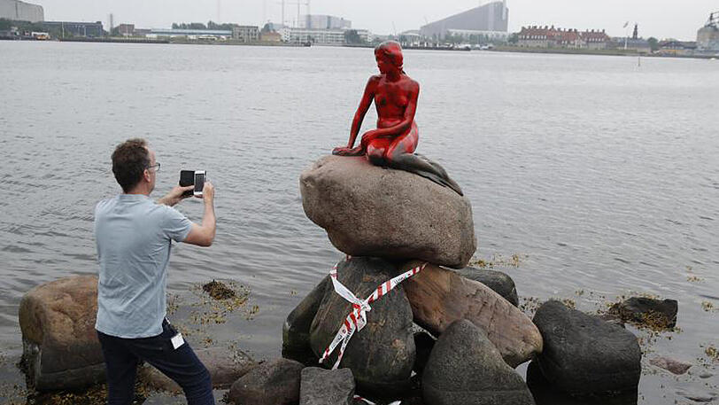 Ein Mann fotografiert die mit roter Farbe beschmierte Statue der kleinen Meerjungfrau im Hafen von Kopenhagen.