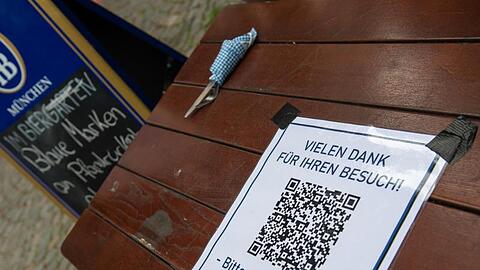 Ein Schild mit einem Barcode klebt auf einem Tisch am Ausgang eines Biergartens. Foto: Peter Kneffel/dpa/Archivbild