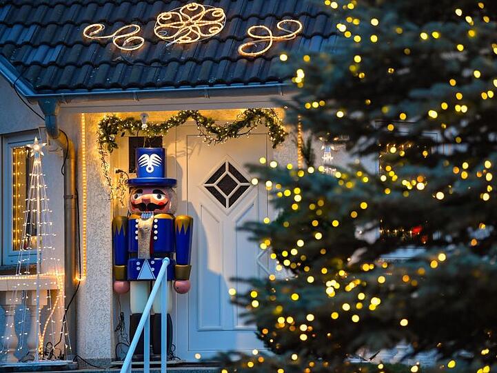 Lichterketten und ein großer Nussknacker stehen an einem weihnachtlich geschmückten Hauseingang.