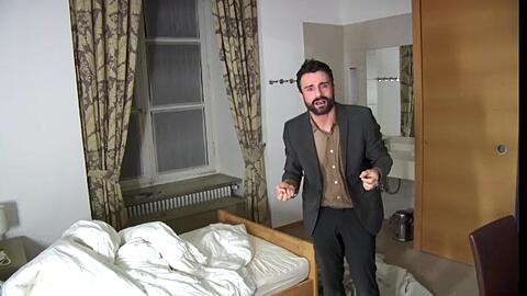 Florian Jahr in Nora Schlockers Zoom-Inszenierung als Superspreader irgendwo in einem eher schäbigen Hotelzimmer.