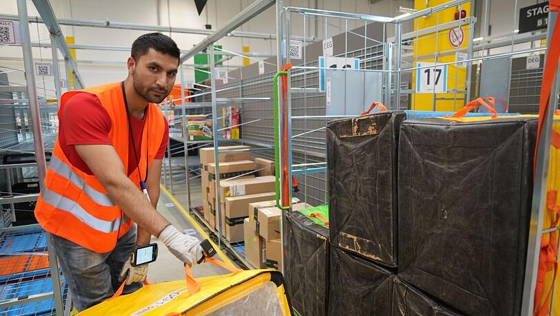 Ein Amazon-Mitarbeiter sortiert per Fingerscanner die Taschen voller Päckchen, die einer internen Farblogik nach auf Wagen gepackt werden. Ein Amazon-Mitarbeiter sortiert per Fingerscanner die Taschen voller Päckchen, die einer internen Farblogik nach auf Wagen gepackt werden.